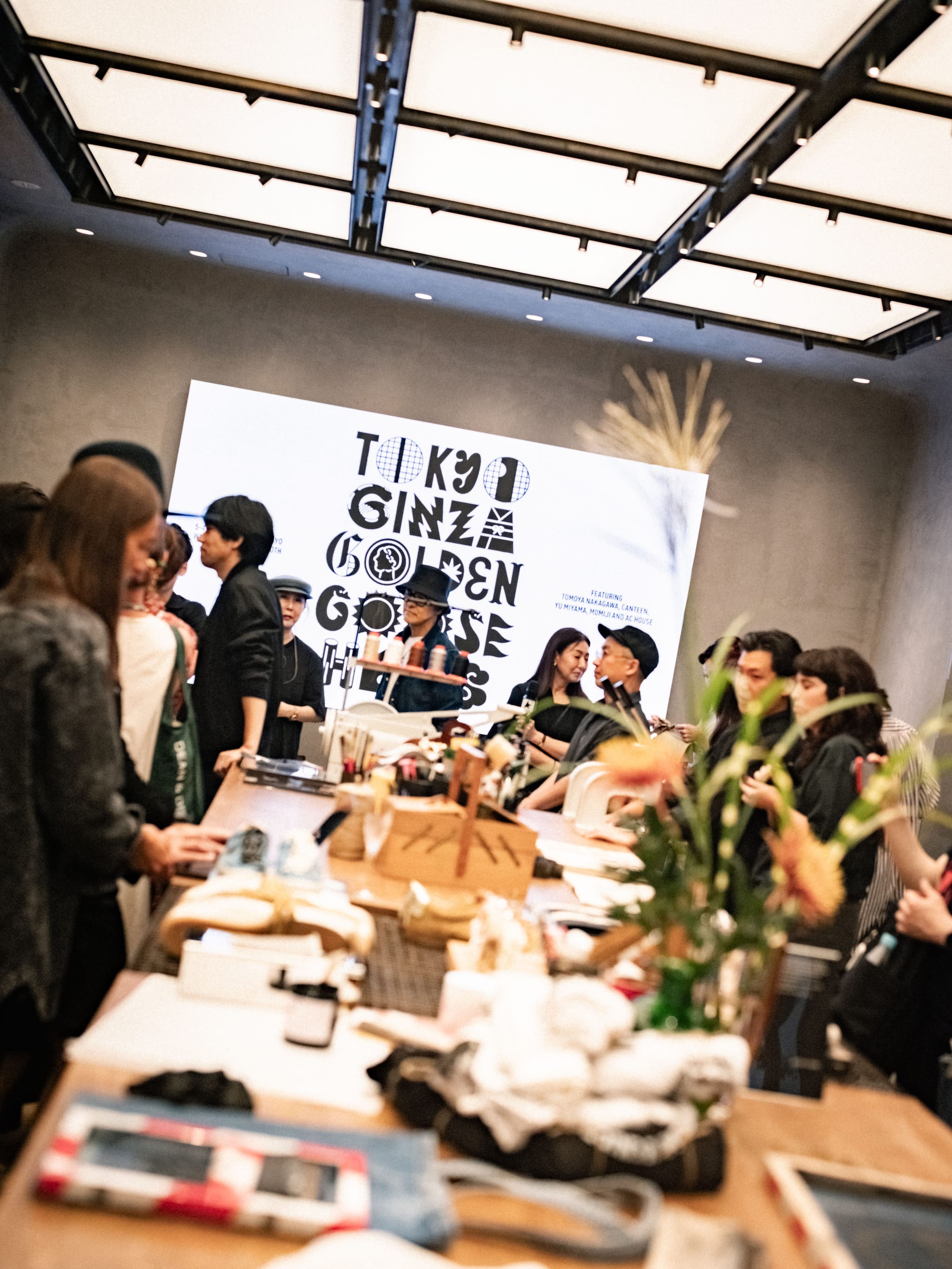 Interior view of lively event with large graphic screen reading Tokyo Ginza Golden Goose Hub