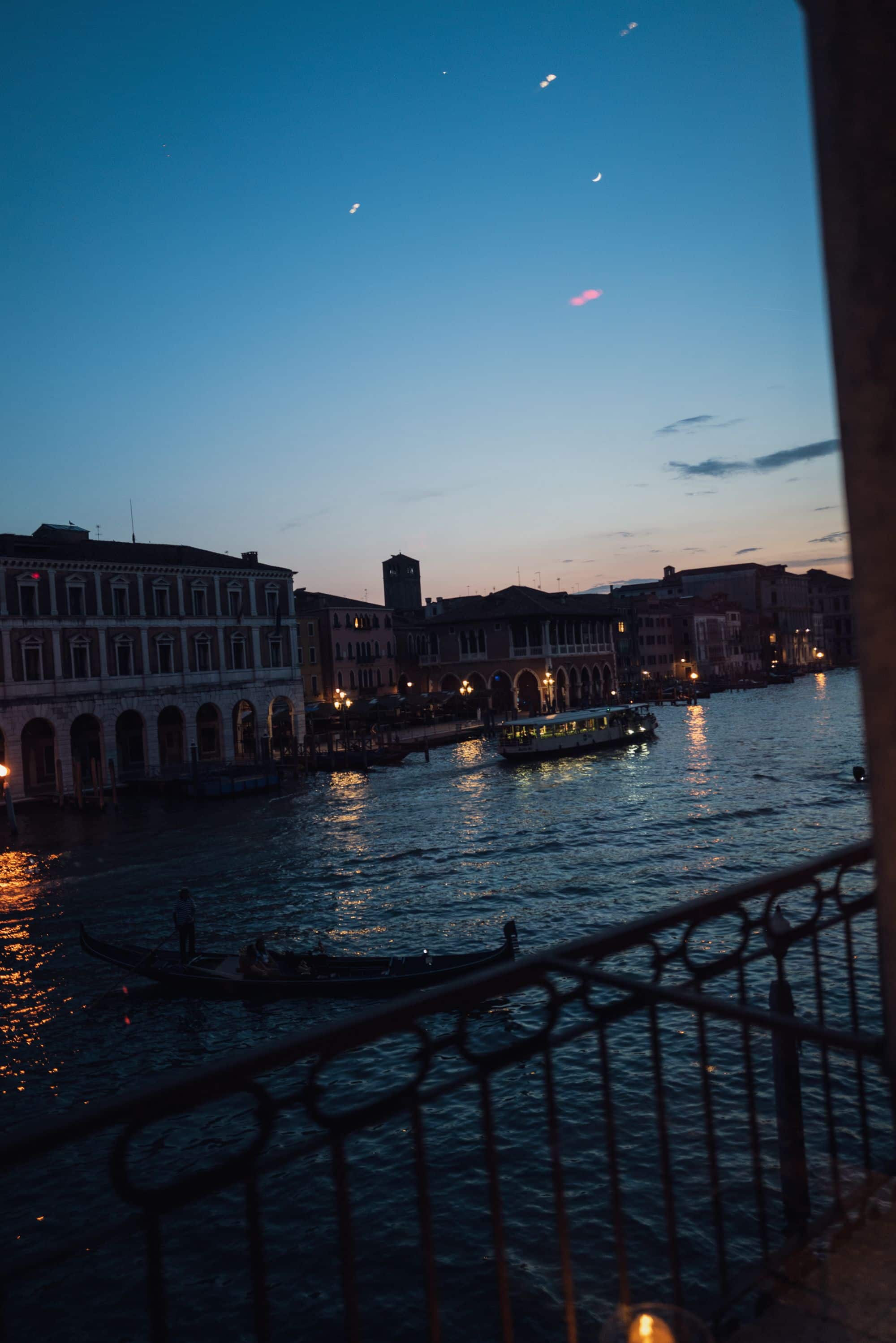 Gondola and vaporetto cruising shimmering water past lit buildings during a peaceful twilight evening in Venice