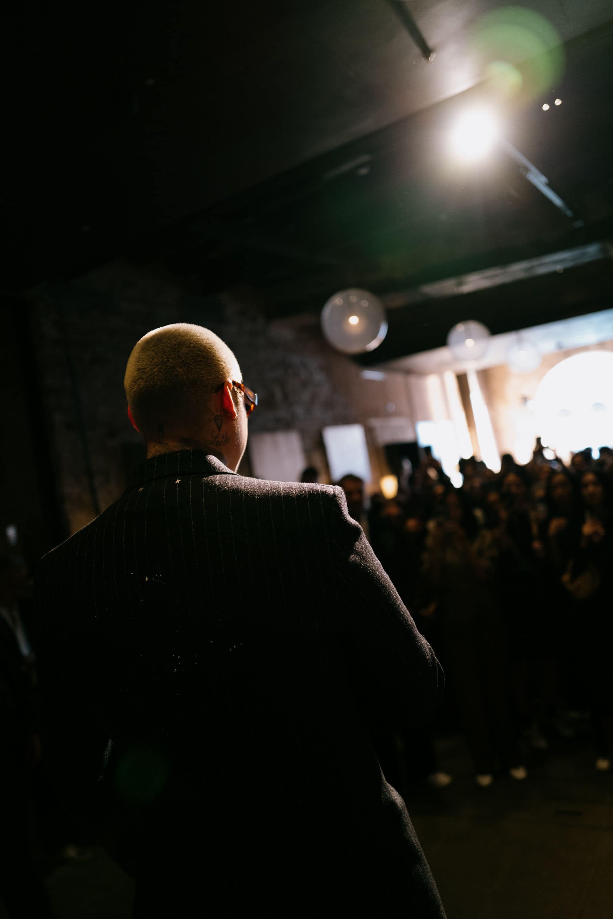 Man in pinstripe suit facing large audience in illuminated venue during Venice Haus event