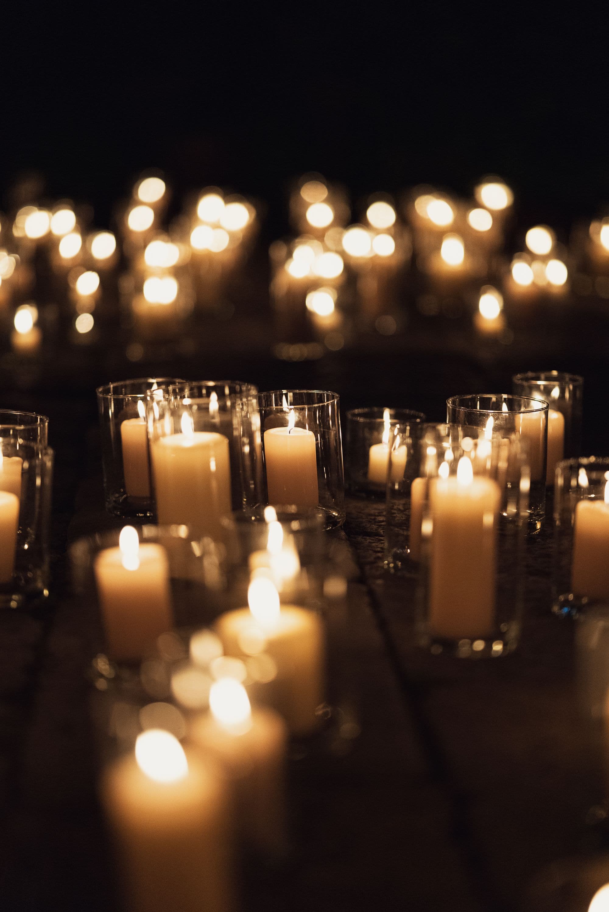 Multiple lit candles arranged in glass jars illuminating dark space at Venice Haus event