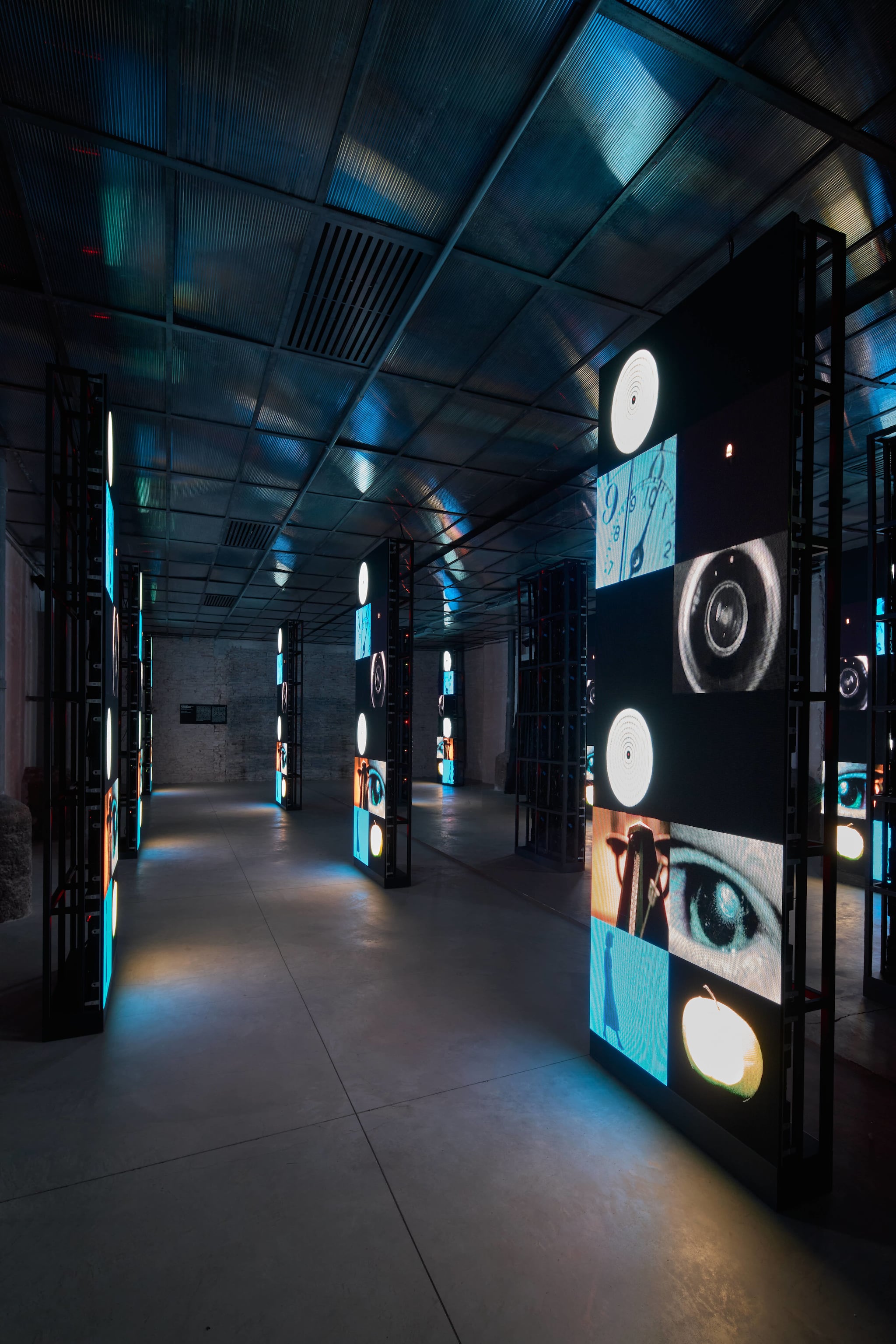 Illuminated vertical pillars displaying diverse digital imagery in dark gallery at Haus event