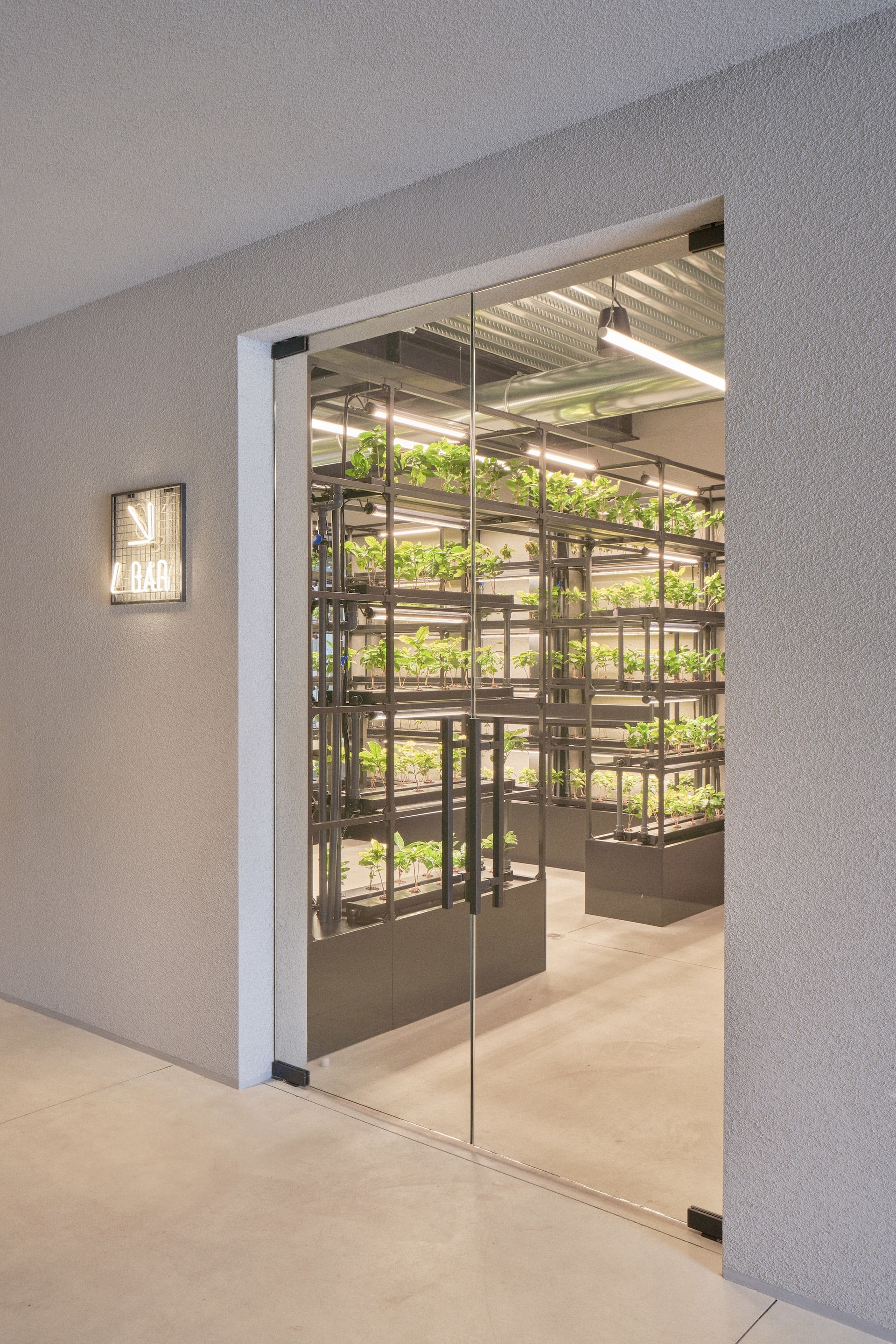 Glass door opening to indoor vertical plant garden near neon sign during Venice Haus tour