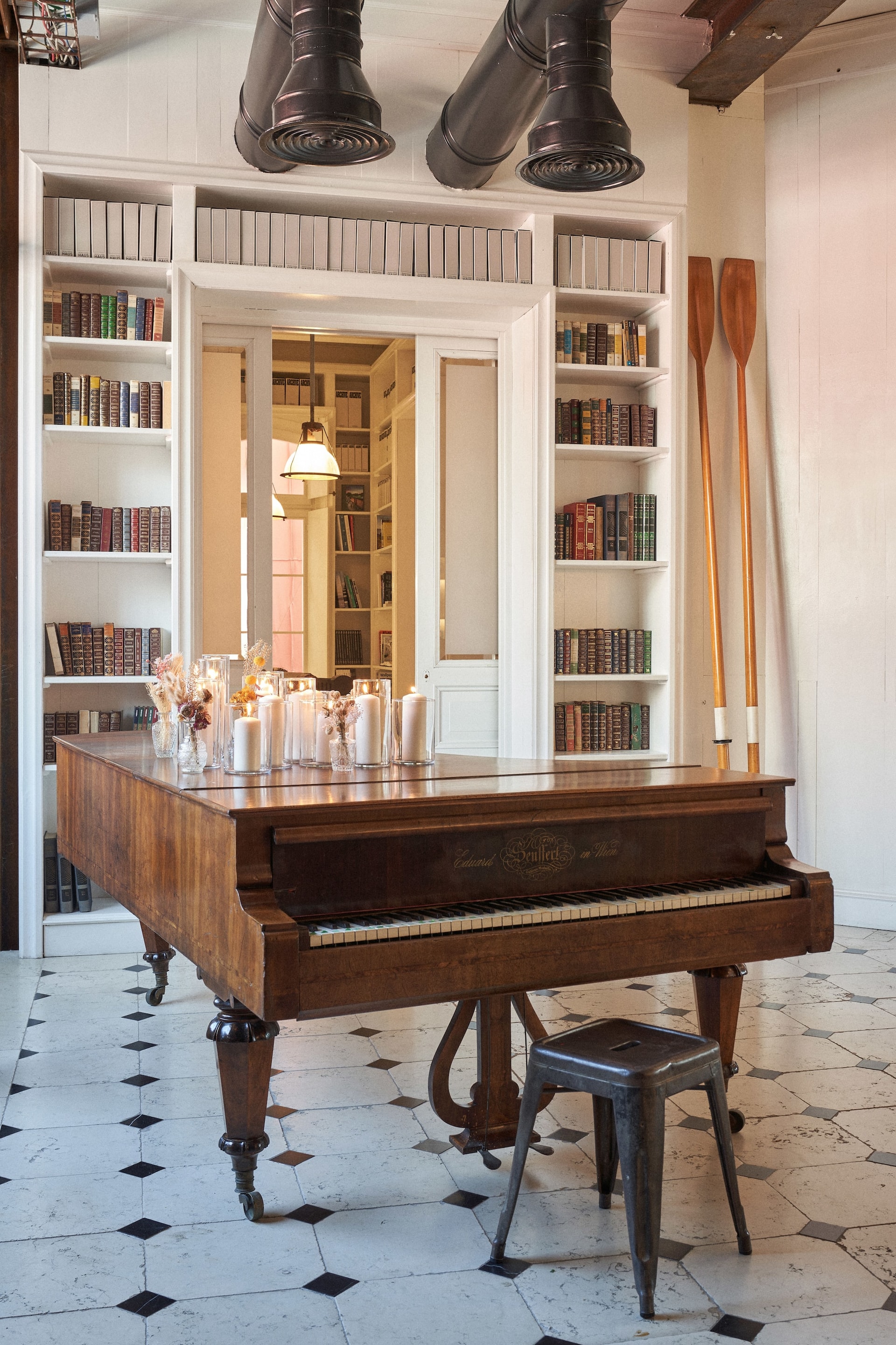 Vintage grand piano decorated with lit candles in front of white bookshelves at Venice Haus location