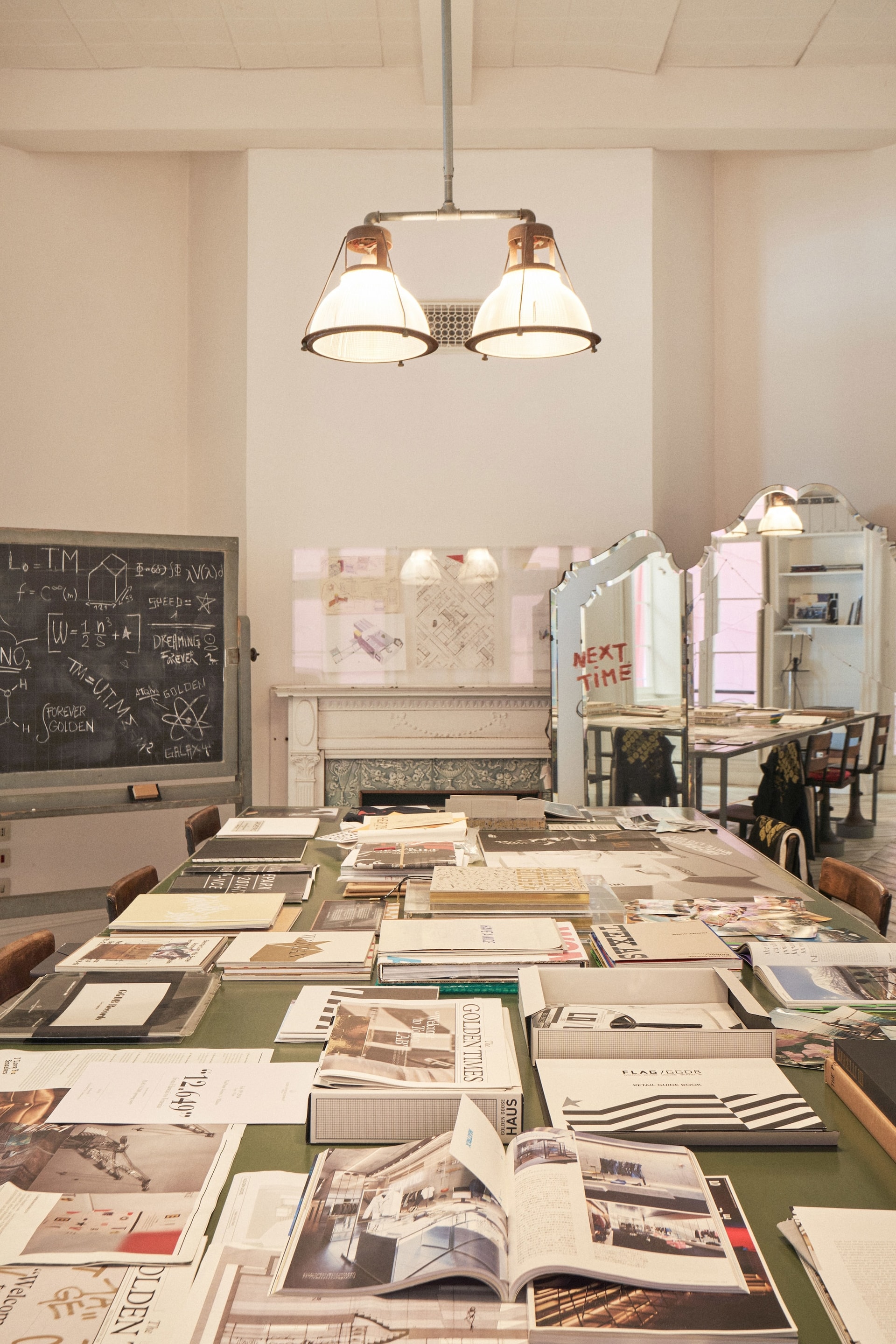 Large table covered with open books and magazines near blackboard in bright room during Venice Haus tour