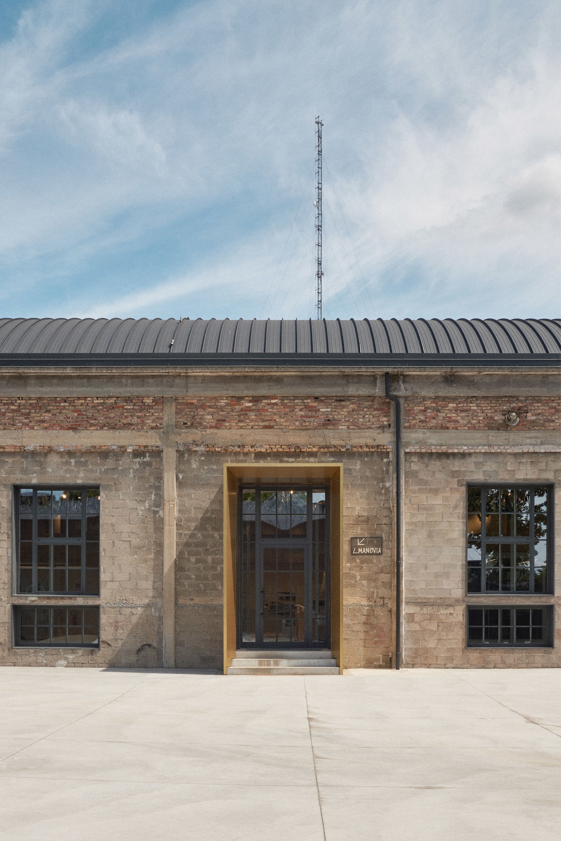 Elegant golden doorway accents a textured brick wall and industrial windows at the Manovia entrance in Venice.