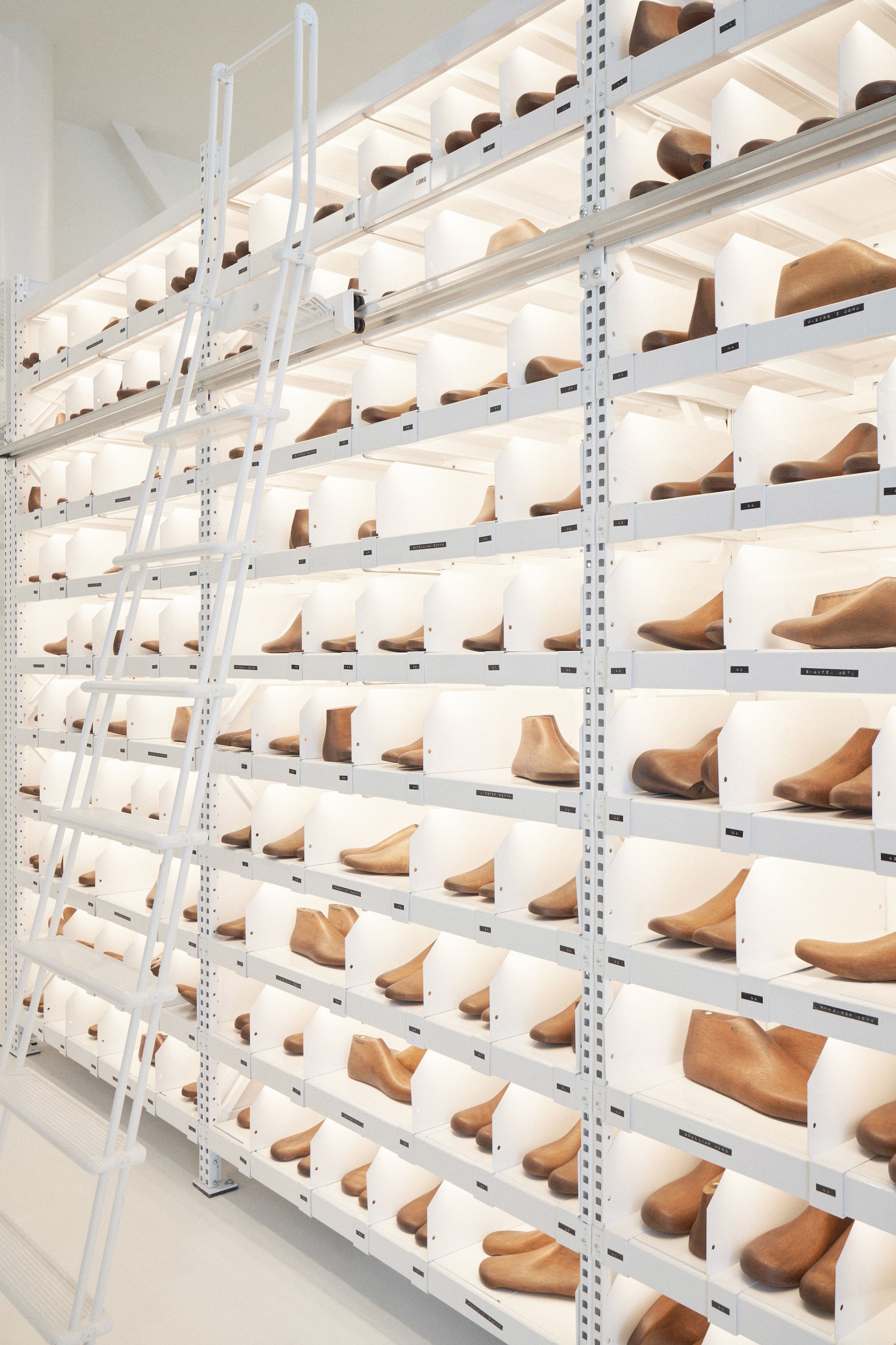 Illuminated floor-to-ceiling shelves at Venice Haus showcase hundreds of wooden shoe lasts with a white rolling ladder.