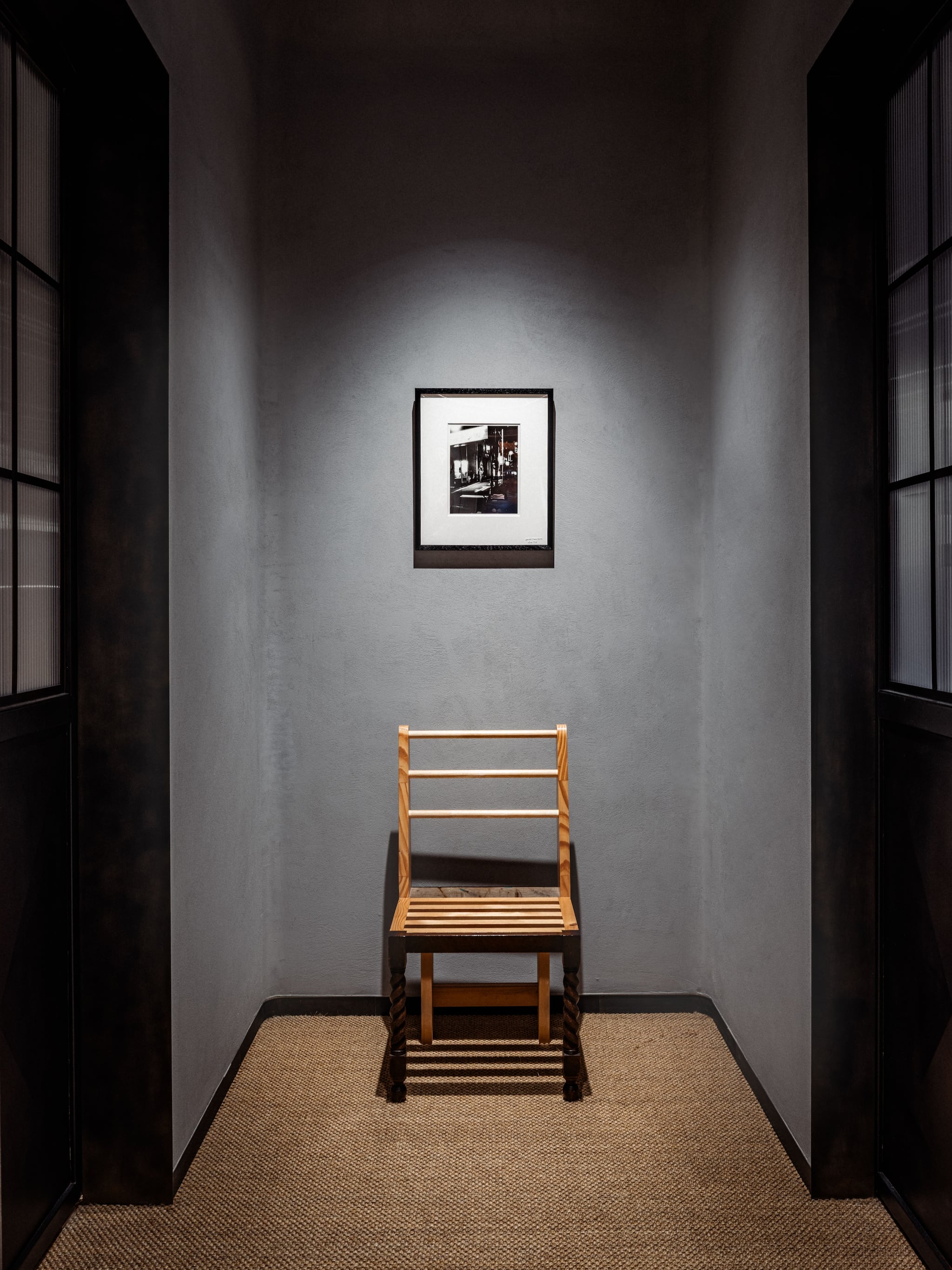 Simple wooden chair under spotlight below framed photo in dark alcove at Tokyo Haus location