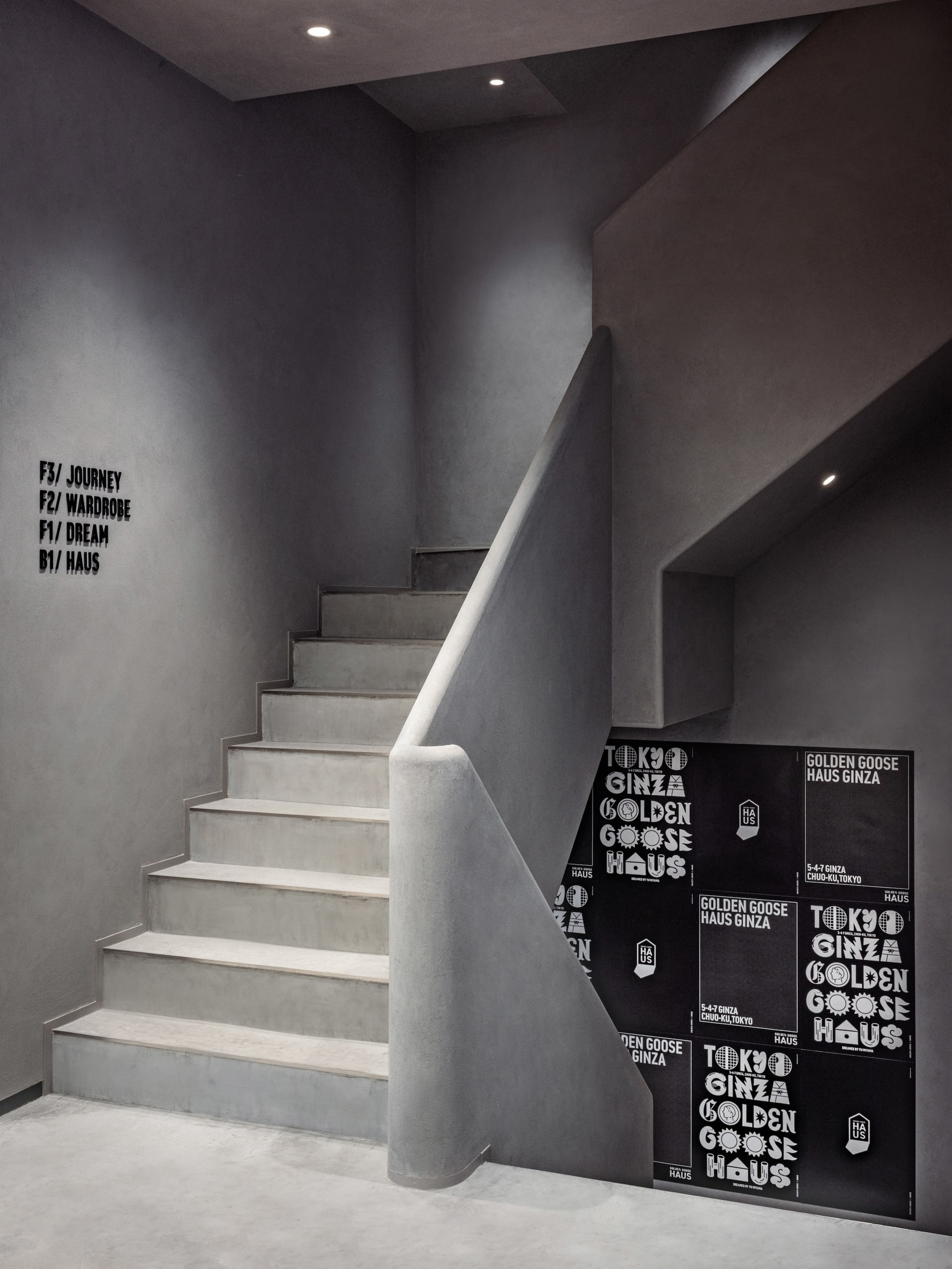 Concrete staircase featuring Golden Goose Haus promotional posters on lower wall at Tokyo Haus location
