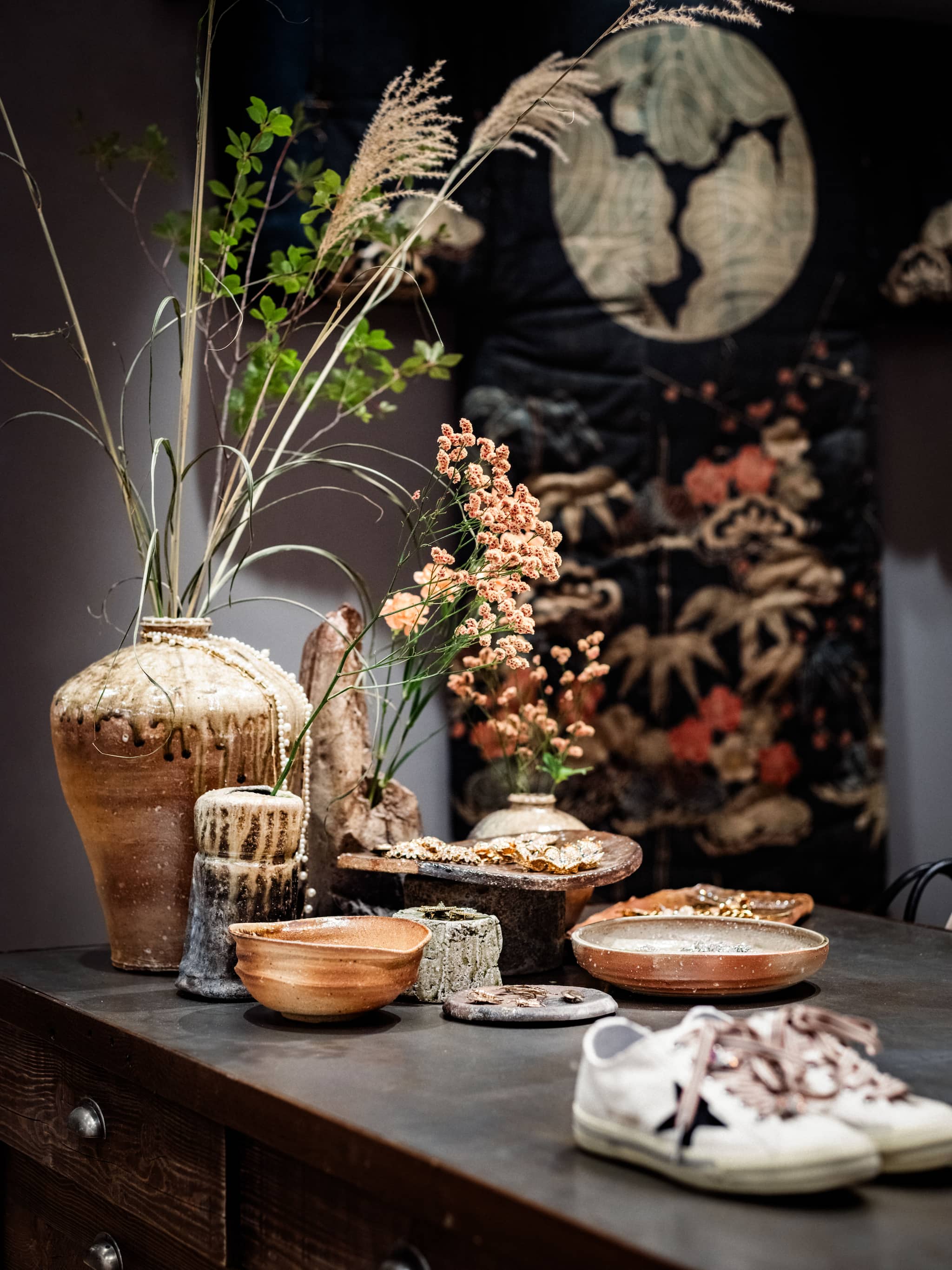 Ceramic vases and dried flowers displayed near jewelry on wooden table at Tokyo Haus location
