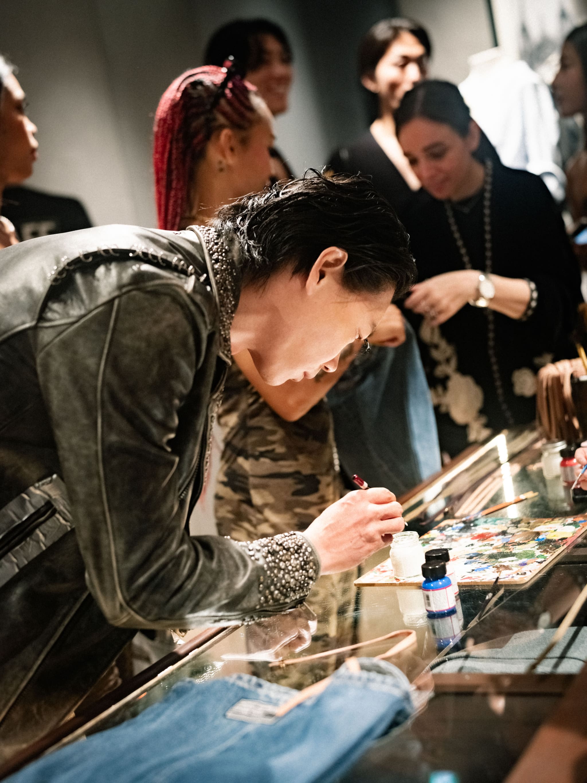 Artist hand-painting on leather jacket on glass table in dark gallery at Tokyo Haus event