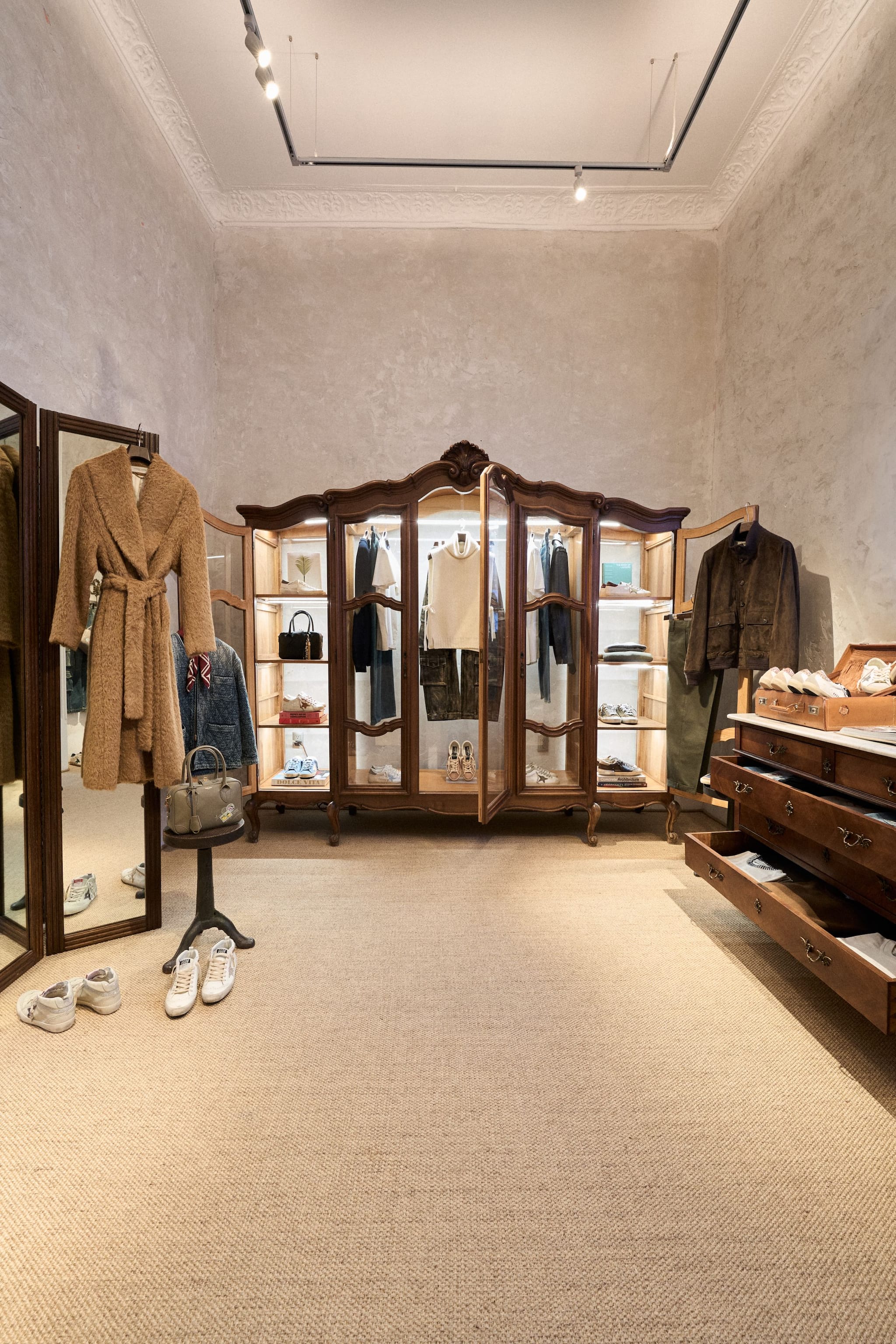Illuminated antique wooden wardrobe displaying clothes in minimalist room with dresser at Mexico Haus location